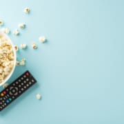 Enjoy home cinema with premieres using TV app. Top-view shot of popcorn, and remote for online viewing on pastel blue backdrop